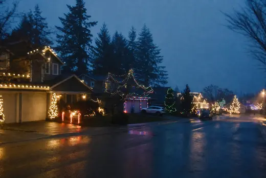 A residential street on a December evening with several houses lit with Christmas lights